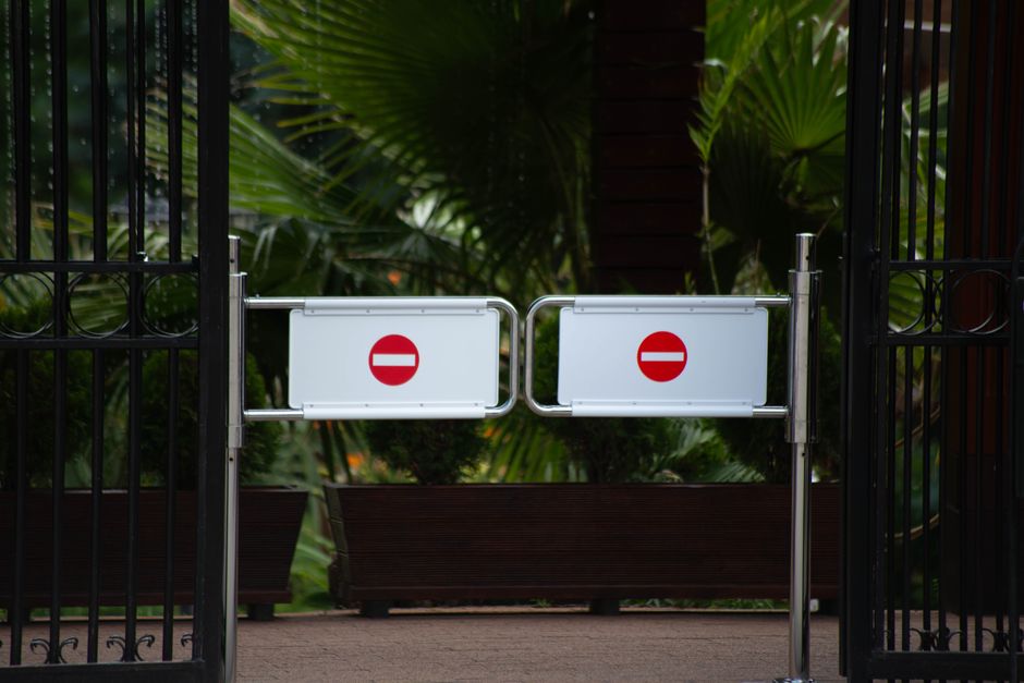 Close-up of a metal gate with two signs attached. The upper sign reads 'NO TRESPASSING' in bold black letters on a white background. The lower sign, also on a white background, displays the message 'U